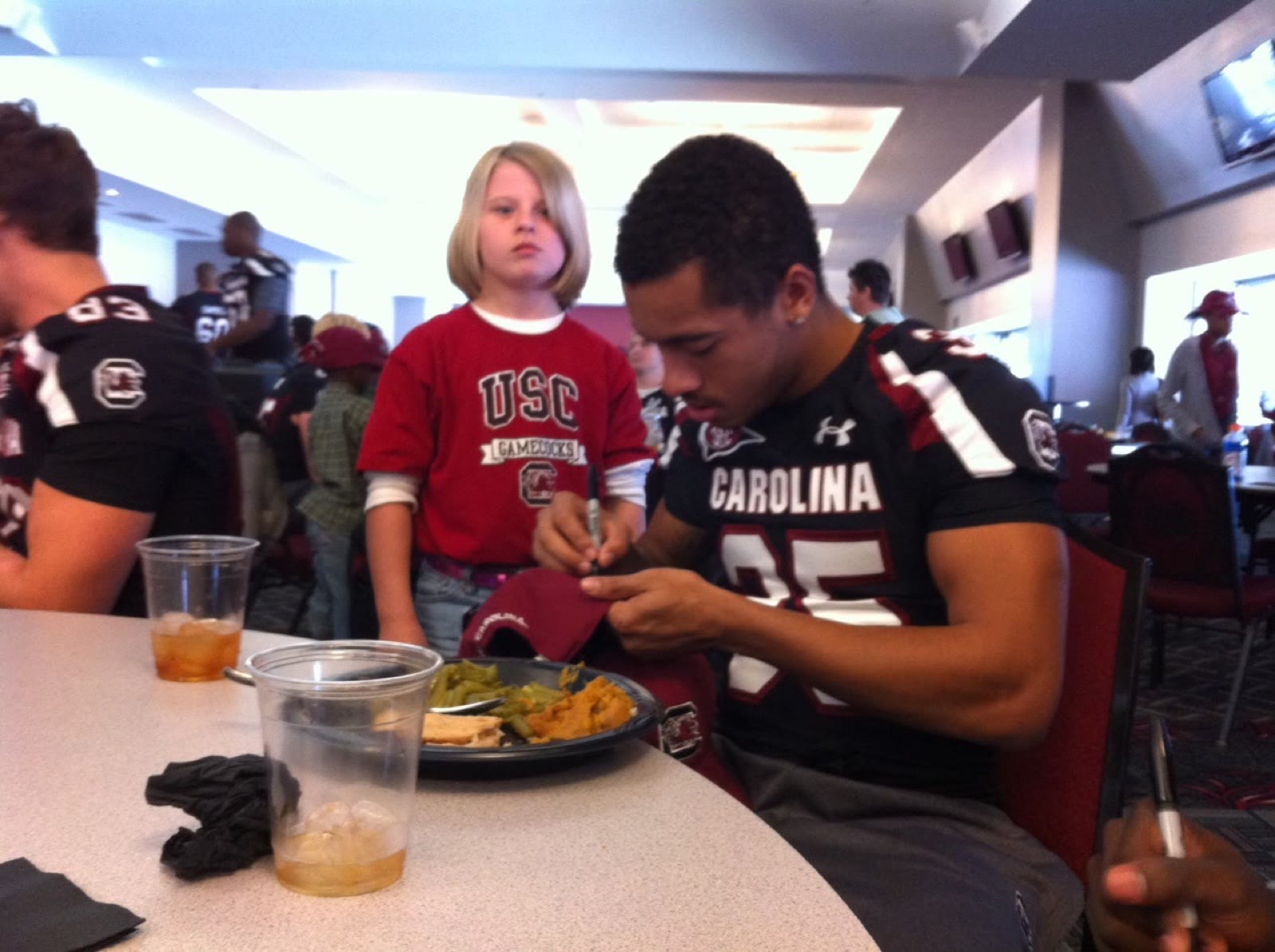 Ben Harvey in a Carolina game jersey signing a cap for a young fan after a game