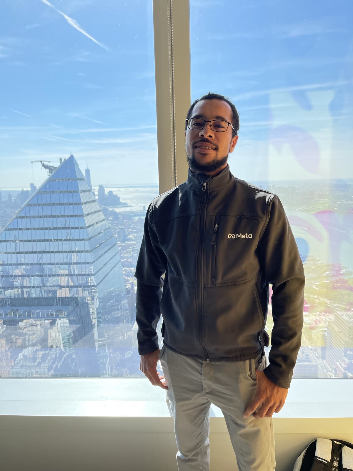 Ben Harvey in a Meta jacket on the top floor of Meta's New York office with the Manhattan skyline behind him